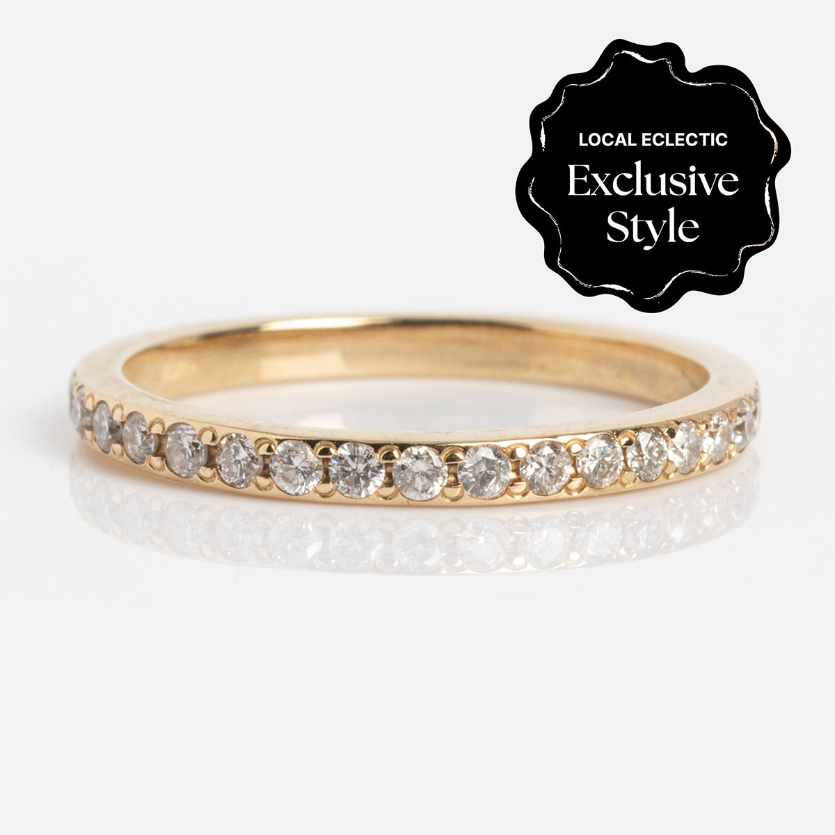 The Infini Diamond Band is a slim 1.5 mm gold ring adorned with a row of sparkling clear diamonds. A black badge in the corner states "Local Eclectic Exclusive Style" against a plain white background.