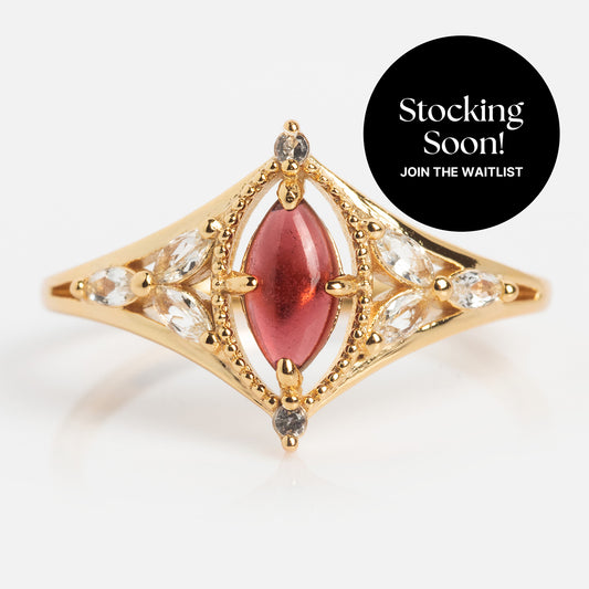 The 2026 January Capsule Art Deco Garnet Ring is a yellow gold vermeil ring with a marquise-shaped red garnet and clear stones in an ornate setting. A black circle says “Stocking Soon! Join the waitlist!”.