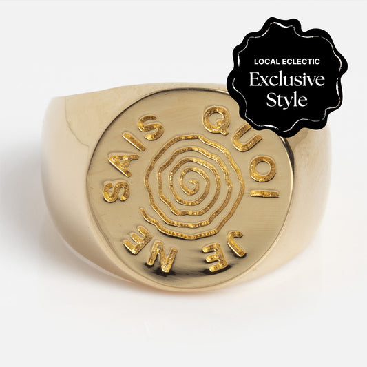 The I Like It Here Club x Local Eclectic Je Ne Sais Quoi Pinky Ring is a gold signet ring with a central spiral design and “JE NE SAIS QUOI” engraved, marked as a Local Eclectic Exclusive Style.