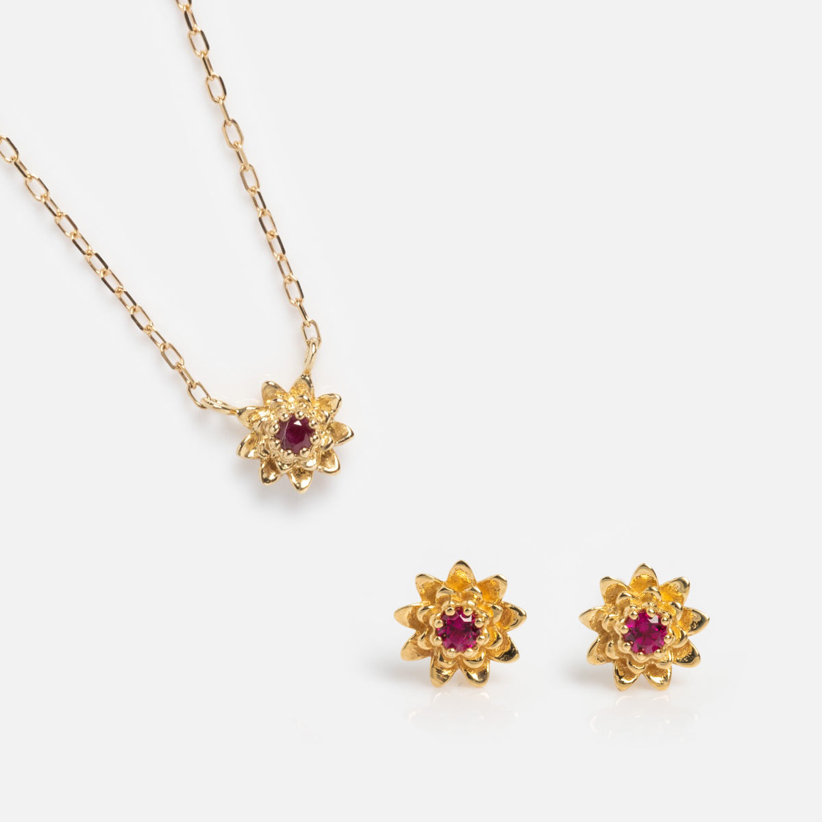 The Solid Gold Birth Flower Gift Set features a flower-shaped necklace and matching earrings with red gemstone centers, elegantly displayed on a white background.