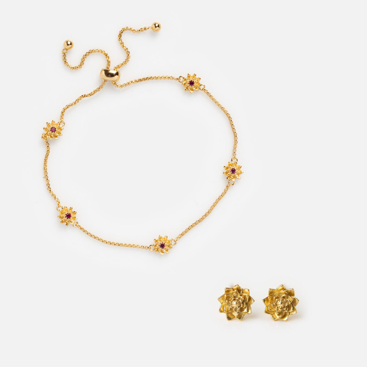 The Birth Flower Gift Set features a gold bracelet with pink and purple flower-shaped charms and matching earrings, showcased on a white background.