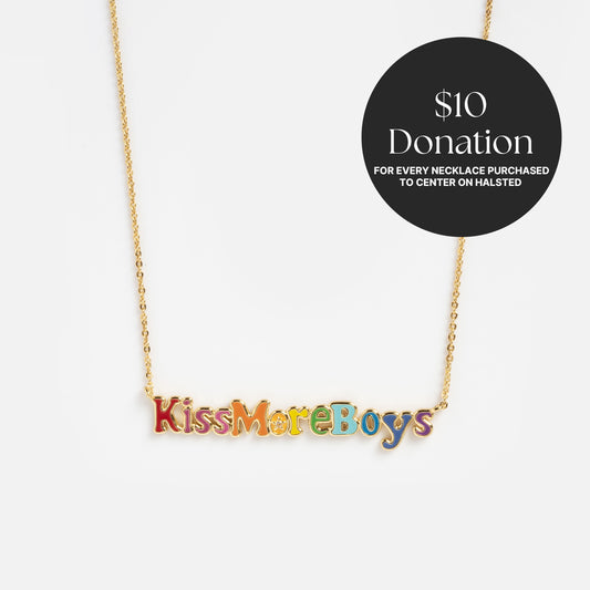 The Kiss More Boys Necklace is a gold chain with colorful "KissMoreBoys" letters. A black circle highlights: $10 from each necklace helps Center on Halsted. Displayed on a white background.
