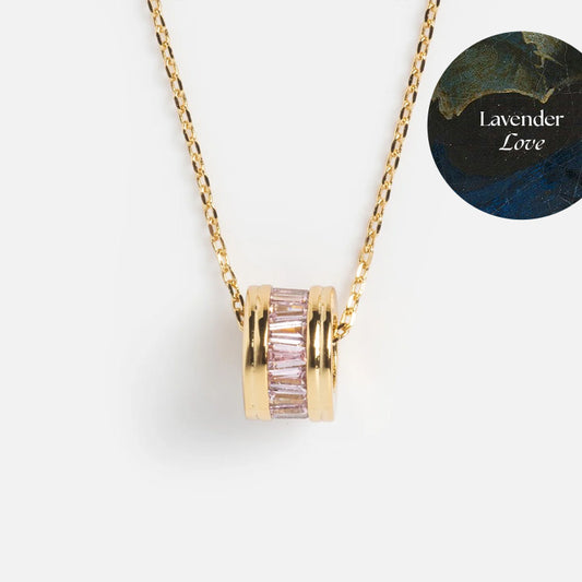 Gold plated Color Theory Charm Necklace with a round pendant adorned with pink baguette-cut CZ stones. A circular label in the top right corner displays Lavender Love on a dark marbled background.