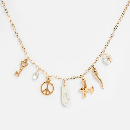 The Goals Charm Necklace features a gold chain with seven charms: a key, clear gem, peace sign, white hand, plane, chili pepper, and clustered freshwater pearls.