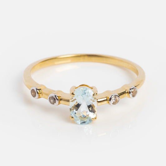 The Solid Gold 2024 March Capsule Classic Aquamarine Ring, Sample Size 10, showcases an oval light blue aquamarine center stone with two small round clear stones on each side, all set in elegant 9k yellow gold and shown on a white background.