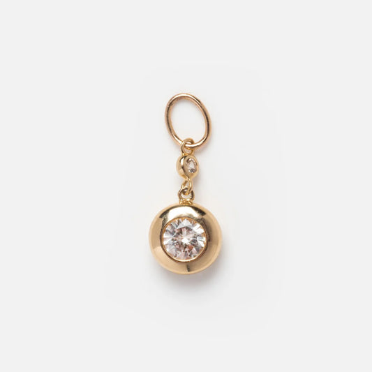 The Solid Gold 2024 April Capsule Classic Diamond Charm features a round, clear diamond at its center, set in gold with a small gold loop and an accent stone above, elegantly displayed on a plain white background.