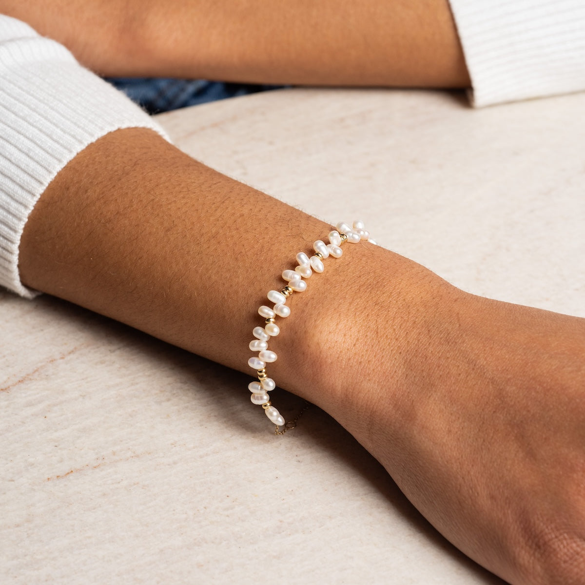 A close-up of a wrist adorned with the Solid Gold Baroque Pearl Bracelet Sample, featuring small white pearls and an extender, worn over a cream-colored sweater against a light background.