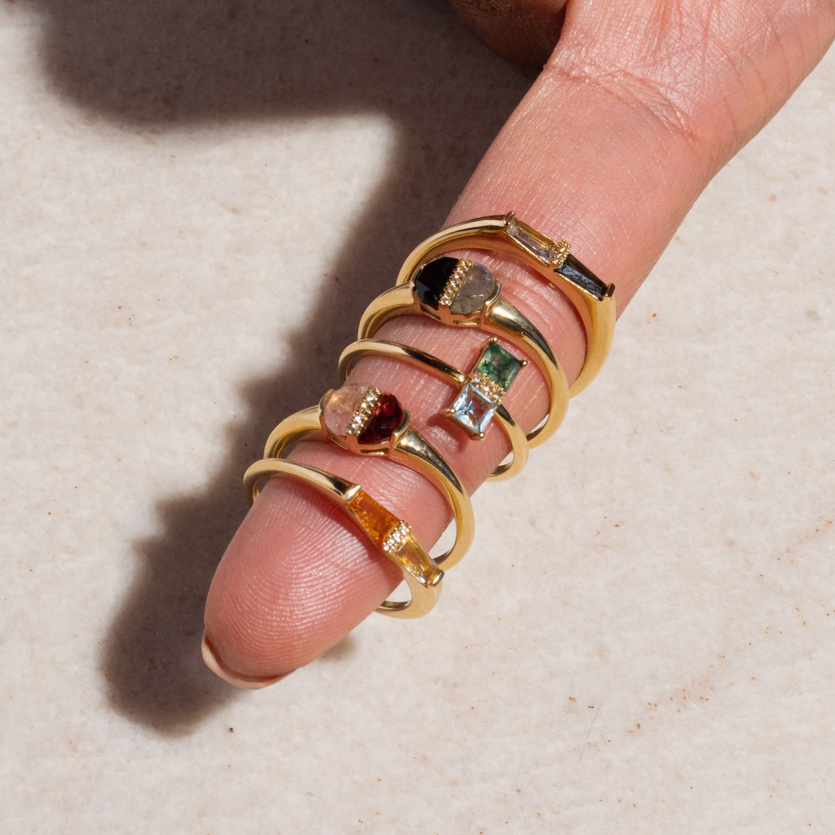 A hand displays the Solid Gold Toi et Moi North South Ring, featuring aquatic agate and blue topaz accents, elegantly stacked on one finger against a light textured background.