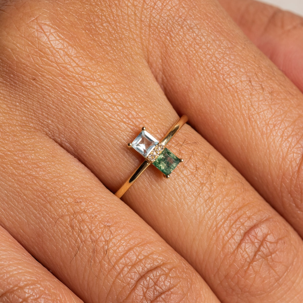 A Solid Gold Toi et Moi North South Ring (size 7) featuring a blue topaz and an aquatic agate, separated by a small row of diamonds, worn on a person's finger.