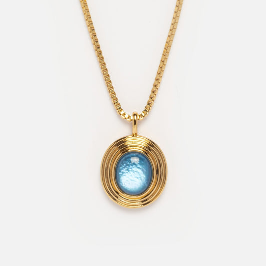 The Saturn Blue Mother of Pearl Pendant Necklace Sample features a 14k yellow gold plated thin box chain and an oval blue gemstone pendant with concentric gold rings, shown against a plain white background.