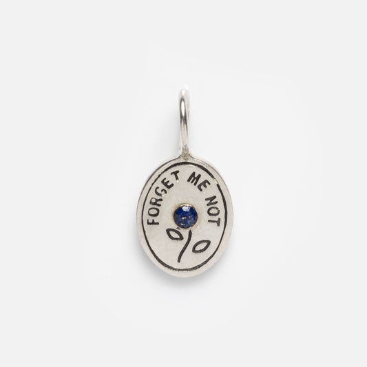 The Charms by Hunt of Hounds in Silver is an oval pendant engraved with FORGET ME NOT, featuring a central blue gemstone and two leaf designs—an empowering, quirky jewelry piece for charm enthusiasts.