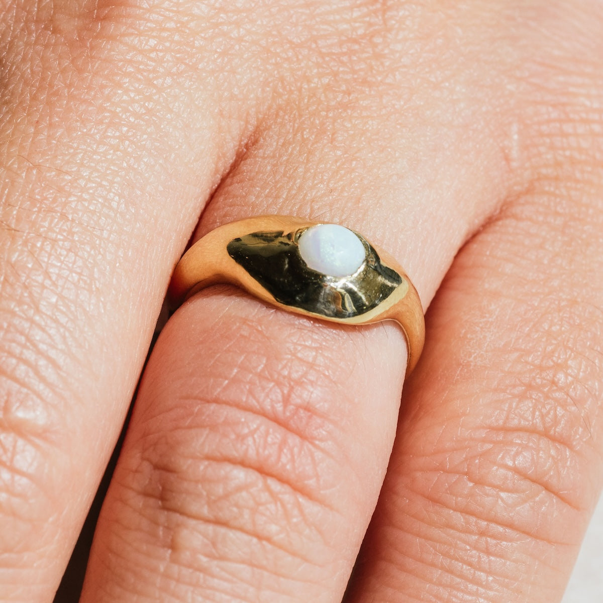 A close-up of a hand wearing the Aether Opal Ring Sample Size 6, featuring a 5 mm round white opal stone set in recycled brass on the middle finger.