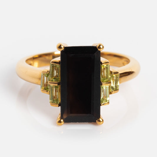 The Bold Baguette Statement Ring in 14k yellow gold plating features a large rectangular black onyx center, accented by three small rectangular light green stones on each side, set against a white background.