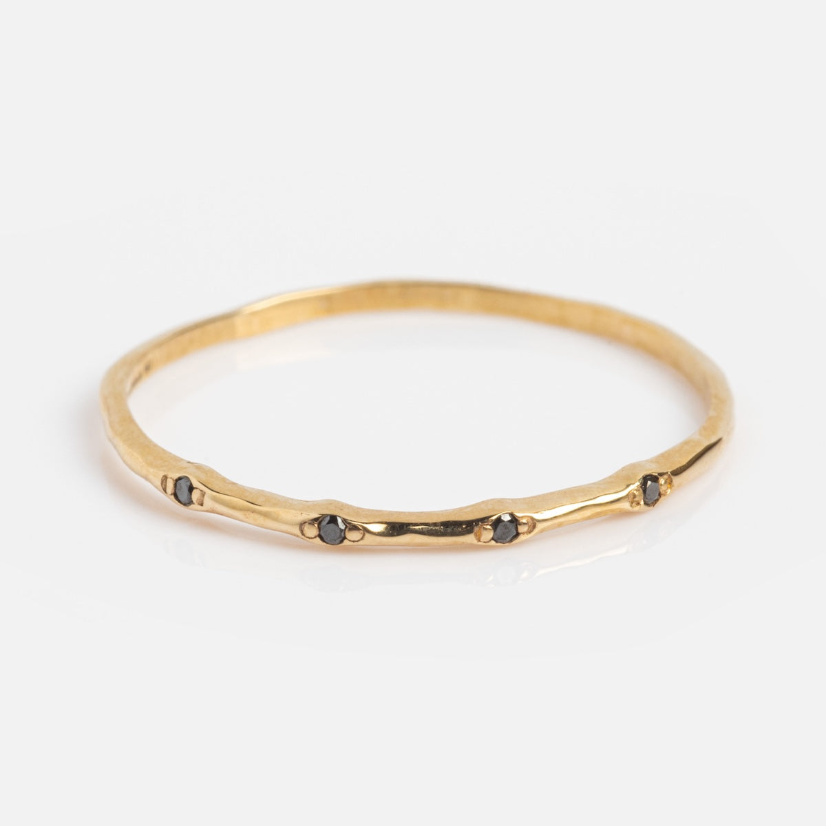 The Solid Gold Textured Diamond Band is a thin, textured 14k yellow gold ring with small black stones set at intervals around the band, shown on a white background.