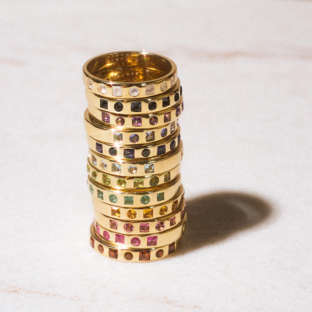 A Solid Gold Within You Birthstone Band in sample size 7, crafted from 9k yellow gold and set with colorful gemstones, rests on light marble. The elegant band is 3.1 mm wide and casts a soft shadow to the right.