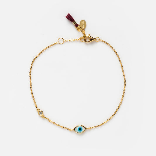 The Madison Evil Eye Bracelet is a 14k vermeil piece featuring a blue evil eye charm, clear gemstone accent, maroon tassel, and gold tags near the clasp—an elegant protective accessory displayed on a white background.