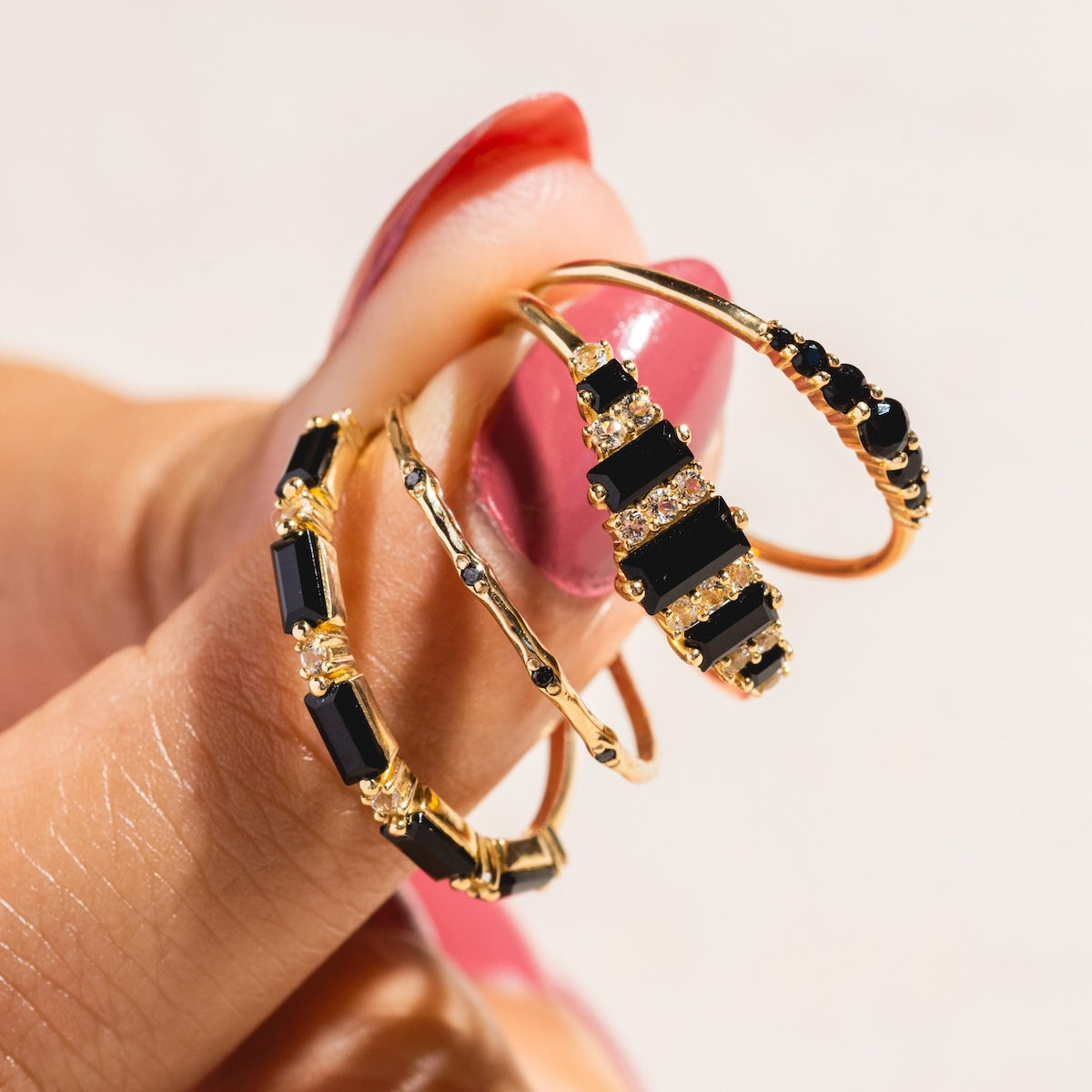 A hand with pink, glossy nails displays a Solid Gold Textured Diamond Band—a 14k yellow gold ring featuring sparkling diamonds—set against a softly blurred background.