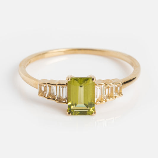 The Solid Gold 2024 August Capsule Classic Peridot Ring features a rectangular green peridot center stone with three baguette-cut clear stones on each side, photographed on a plain white background.