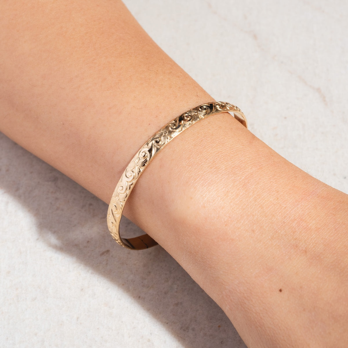A close-up of a wrist wearing the handmade Goddess Cuff Sample, a gold filled bracelet with intricate floral patterns, crafted in Costa Mesa, shown against a light textured background.
