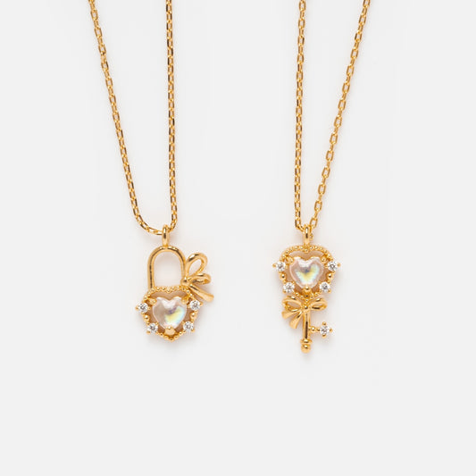 The Forever and Always Necklace Set Sample features two 18k yellow gold plated necklaces: one with a heart-shaped lock and bow pendant accented with CZ crystals, the other with a matching key pendant—perfect for layering.