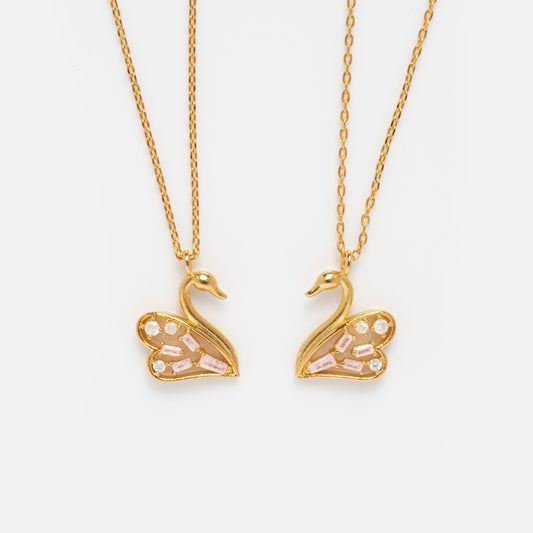 The Swan Lake Necklace Set Sample features two layered necklaces with swan-shaped pendants, crafted in brass and finished with 18k yellow gold plating, showcasing pink and clear gemstone wings against a white background.