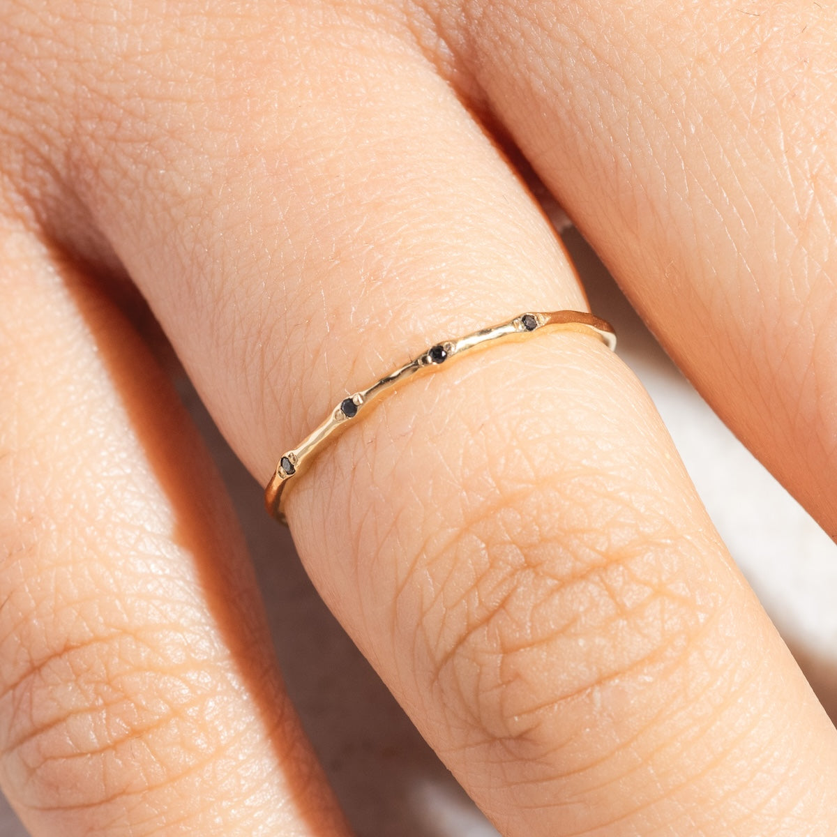 A close-up of a hand wearing the Solid Gold Textured Diamond Band, crafted in 14k yellow gold with shimmering diamonds along a thin band, displayed against a natural light skin tone background.