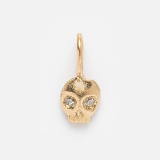 The 14k Solid Gold Tiny Charms by Acanthus features a small yellow gold skull-shaped pendant with two clear gemstone eyes, shown on a white background—ideal for lovers of unique gold and gemstone jewelry.
