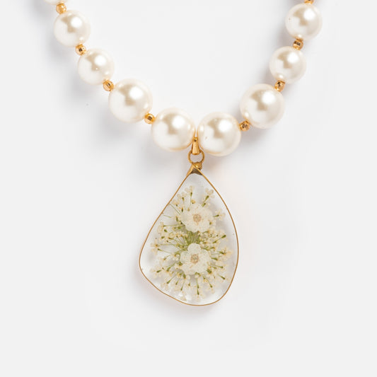 A close-up shows the Penelope Necklace, a handmade beaded pearl piece with a teardrop-shaped pendant featuring a delicate white flower encased in clear resin and outlined by a gold border.