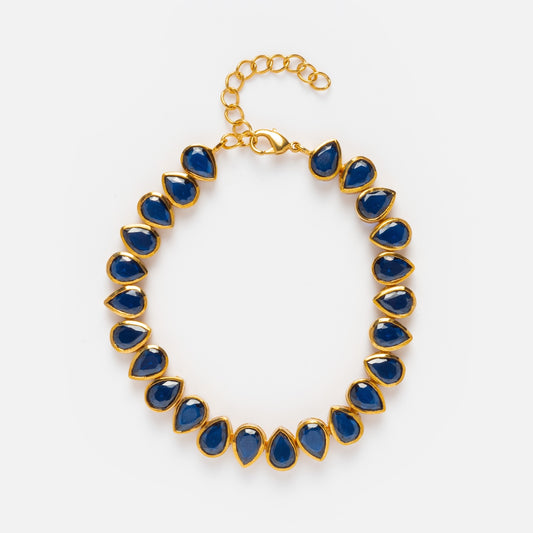 The Bezel Set Birthstone Tennis Bracelet features teardrop-shaped blue gemstones, each bezel set in gold and evenly spaced, with an adjustable clasp and extension chain for a perfect fit.