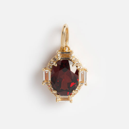 The Solid Gold Vintage Inspired Birthstone Charm showcases an oval deep red gemstone at the center, encircled by small clear stones and rectangular accents, all set in solid gold on a plain white background.