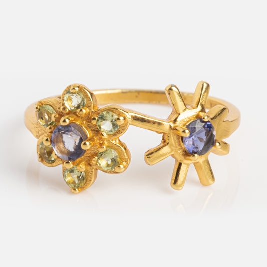 The Sungoddess Ring Sample Size 6 is a yellow gold plated ring with two floral designs: one features green peridot petals and a purple center; the other has a gold outline with a purple iolite gemstone in the center, shown on a white background.