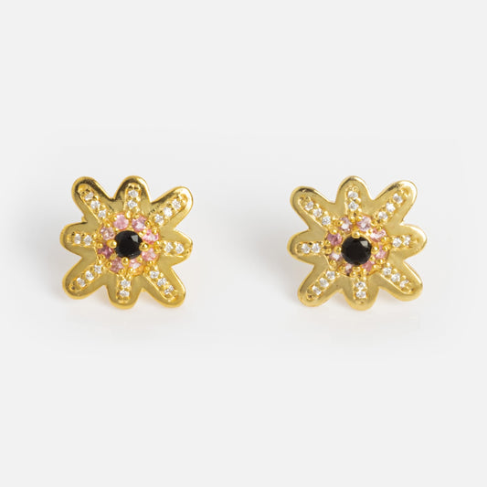The Wildbloom Stud Earrings Sample features flower-shaped studs in 18k yellow gold plating with pink tourmaline, clear gemstones, and a black chalcedony center, shown on a plain white background.