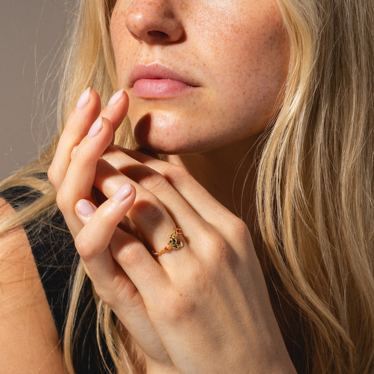 A close-up of a woman with long blonde hair and freckles, wearing a black top and a Disney Zero Adjustable Ring, her fingers gently touching her lips and face as she gazes thoughtfully.