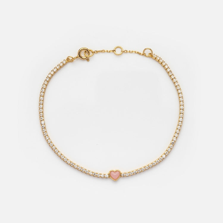 The Coral Heart Diamond Tennis Bracelet Sample features a row of simulated diamonds and a central pink heart charm on an 18k gold vermeil chain, shown against a plain white background.