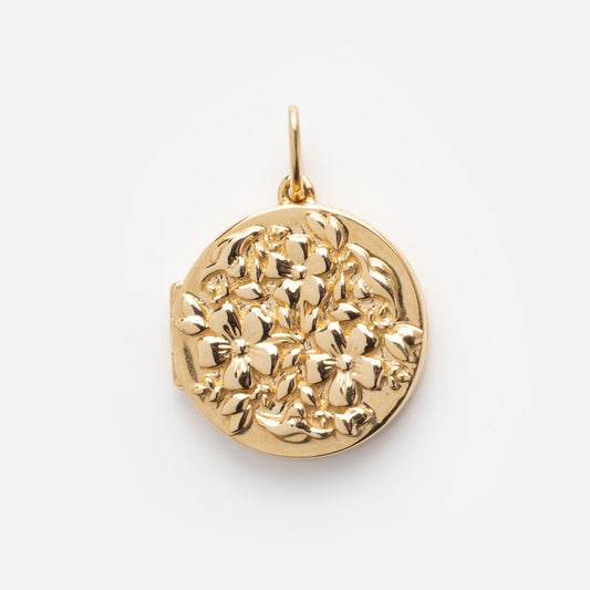 The Solid Gold Locket Charm is a round locket with a raised floral design, showcasing detailed flowers and leaves on the front, set against a plain white background.