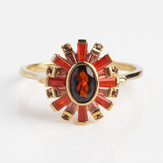 The Solid Gold 2024 January Capsule Vintage Inspired Statement Ring (Sample Size 10) showcases a central oval red garnet with radiating red and pink baguette and round stones in a sunburst pattern, displayed on a white background.
