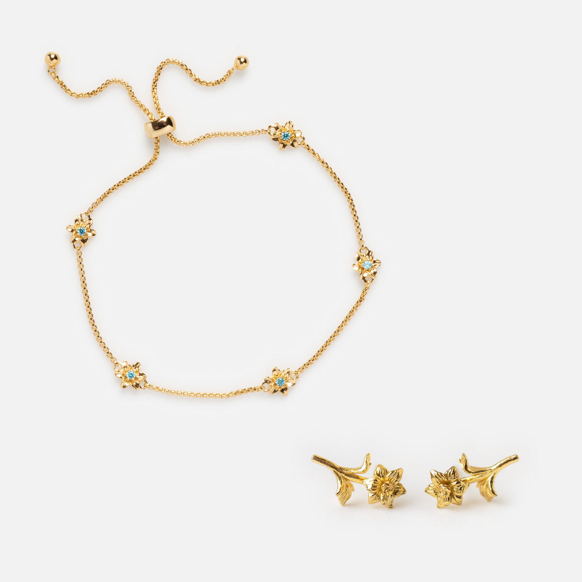 The Birth Flower Gift Set features a gold bracelet with adjustable chain and small blue gemstone flower charms, paired with gold floral stud earrings—ideal as personalized birth flower jewelry.