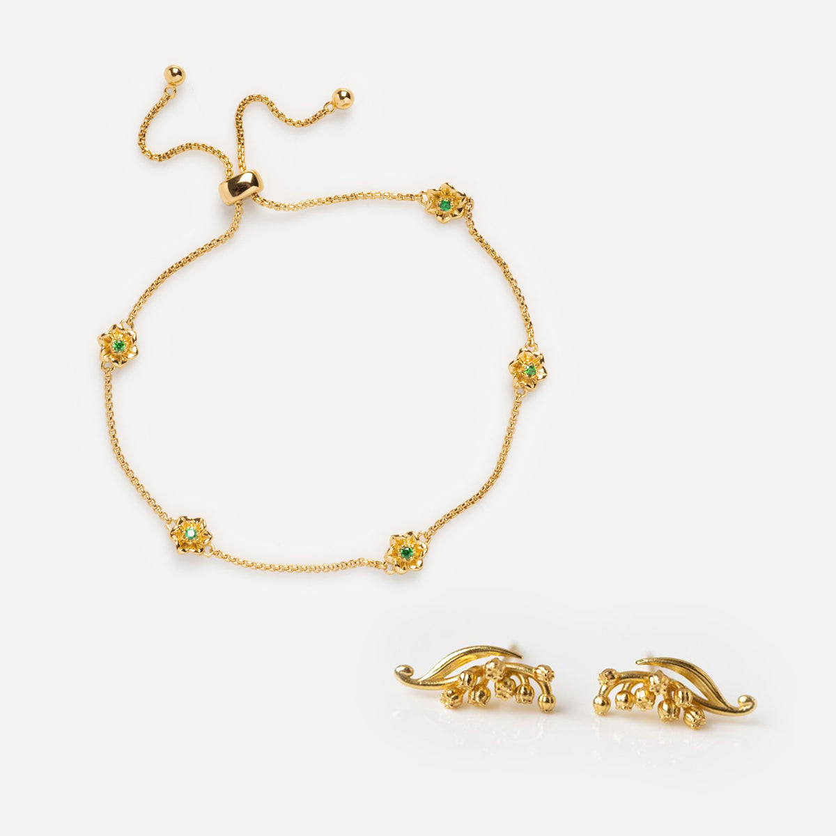 The Birth Flower Gift Set features a gold bracelet with green gemstone flower accents and a sliding clasp, paired with intricately designed birth flower earrings, both elegantly displayed on a plain white background.