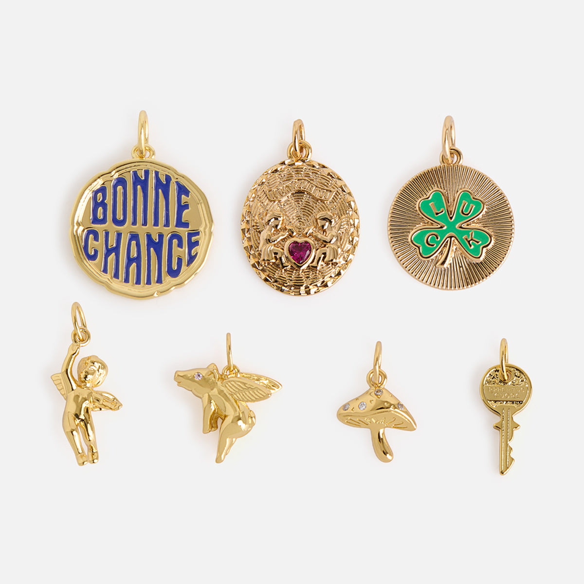 Charms by Mod + Jo features seven 14k gold plated charms on a white background: a Bonne Chance medallion, heart with wings, four-leaf clover, cupid, flying pig, mushroom, and key.