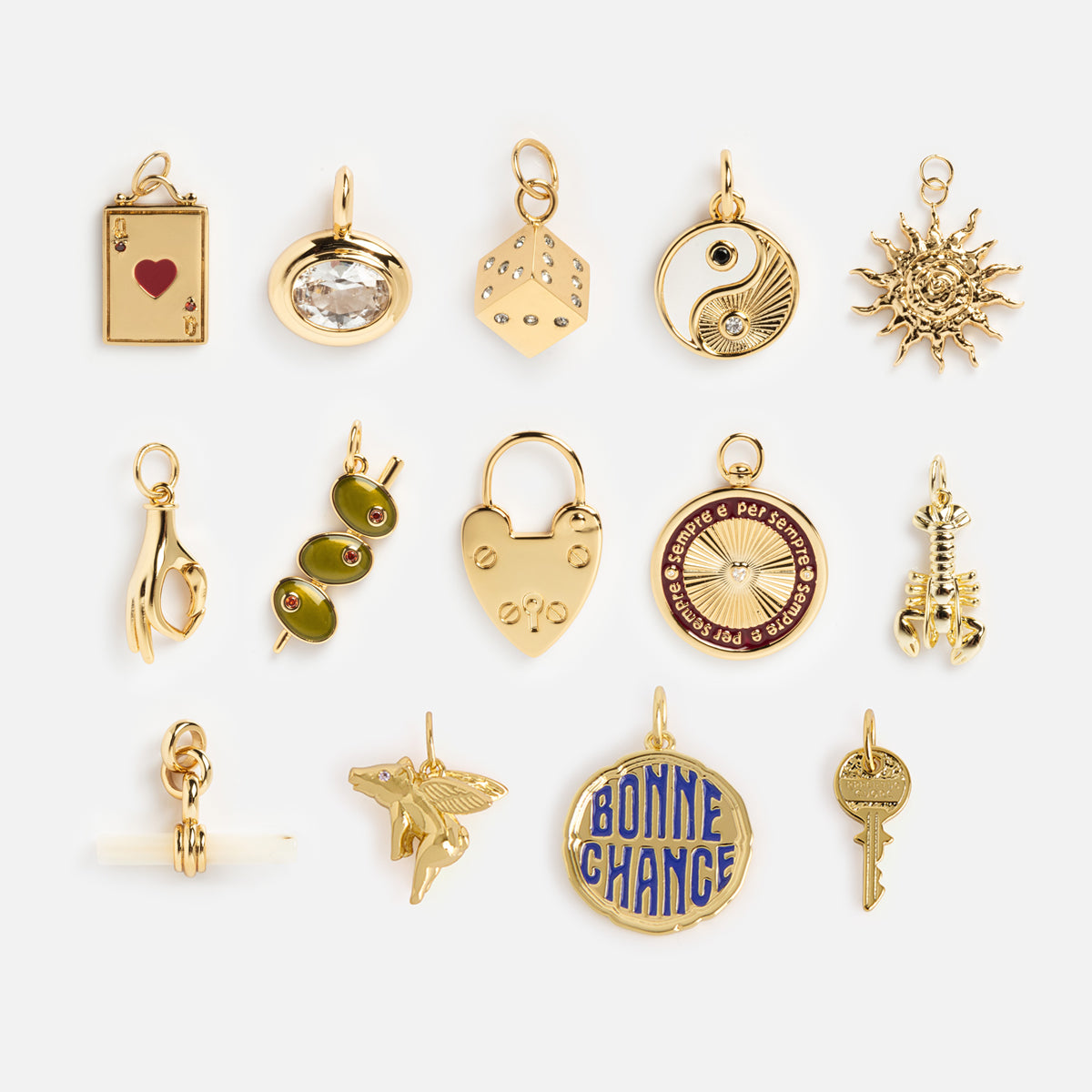 Charms by Mod + Jo: a set of fifteen gold-plated charms, including a heart, lock, sun, yin-yang good luck charm, key, olives, skeleton, book, hand, winged horse, and round medallions on a white background.