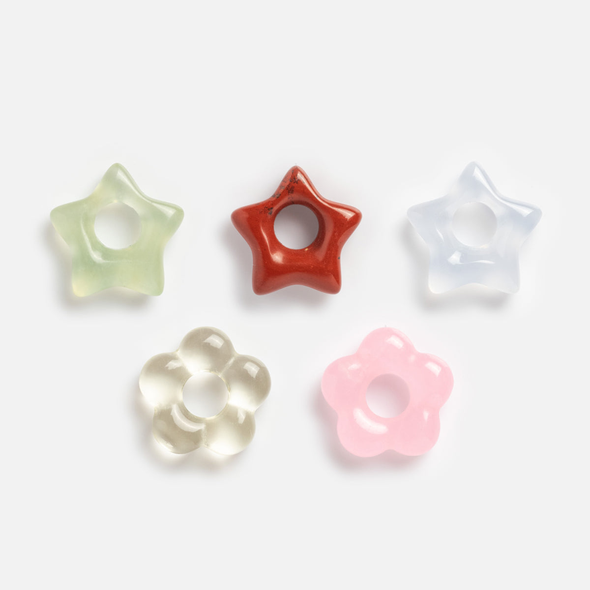 Five Gemstone Spacer Charms by Mod + Jo in pastel green, red, light blue, clear, and pink—shaped like stars and flowers—are neatly arranged on a white background. Perfect for customizable drop earrings.