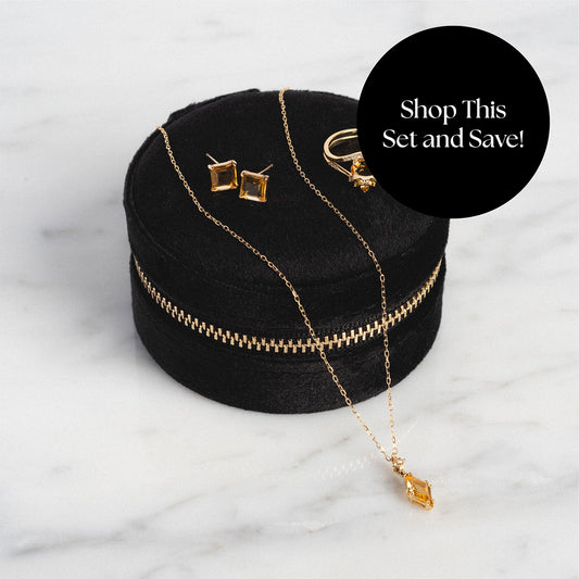 The Solid Gold 2025 November Capsule Citrine Full Set—including necklace, earrings, and ring—is displayed on a round black velvet case. A black circle overlay says, “Shop This Set and Save!” against a white marble background. Comes with a free gift.