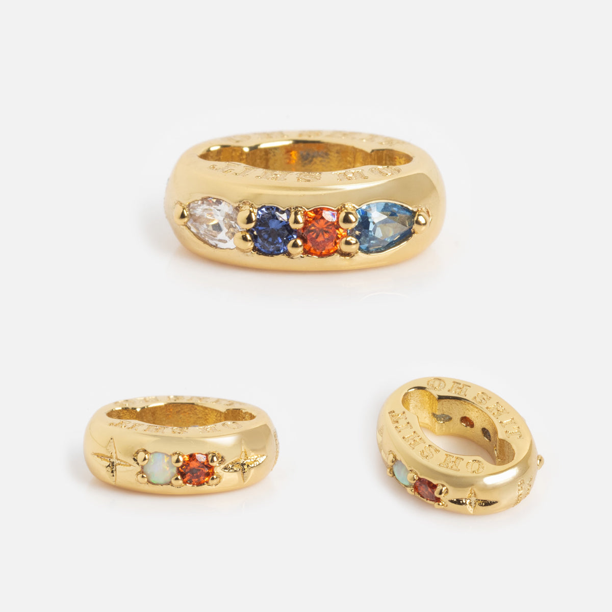 Three views of the Hidden Curse Word Spacer Charm, a chunky gold ring set with five oval gemstones in clear, blue, orange, and green on a white background. The inner band features engraved text.