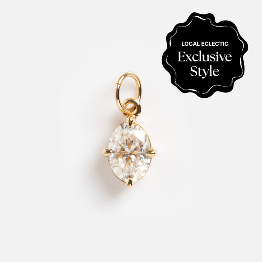The One of a Kind 14k Oval Moissanite Charm features an oval-shaped clear moissanite in a prong setting with hand engraved details, displayed on white. A black badge reads Local Eclectic Exclusive Style at the top right.