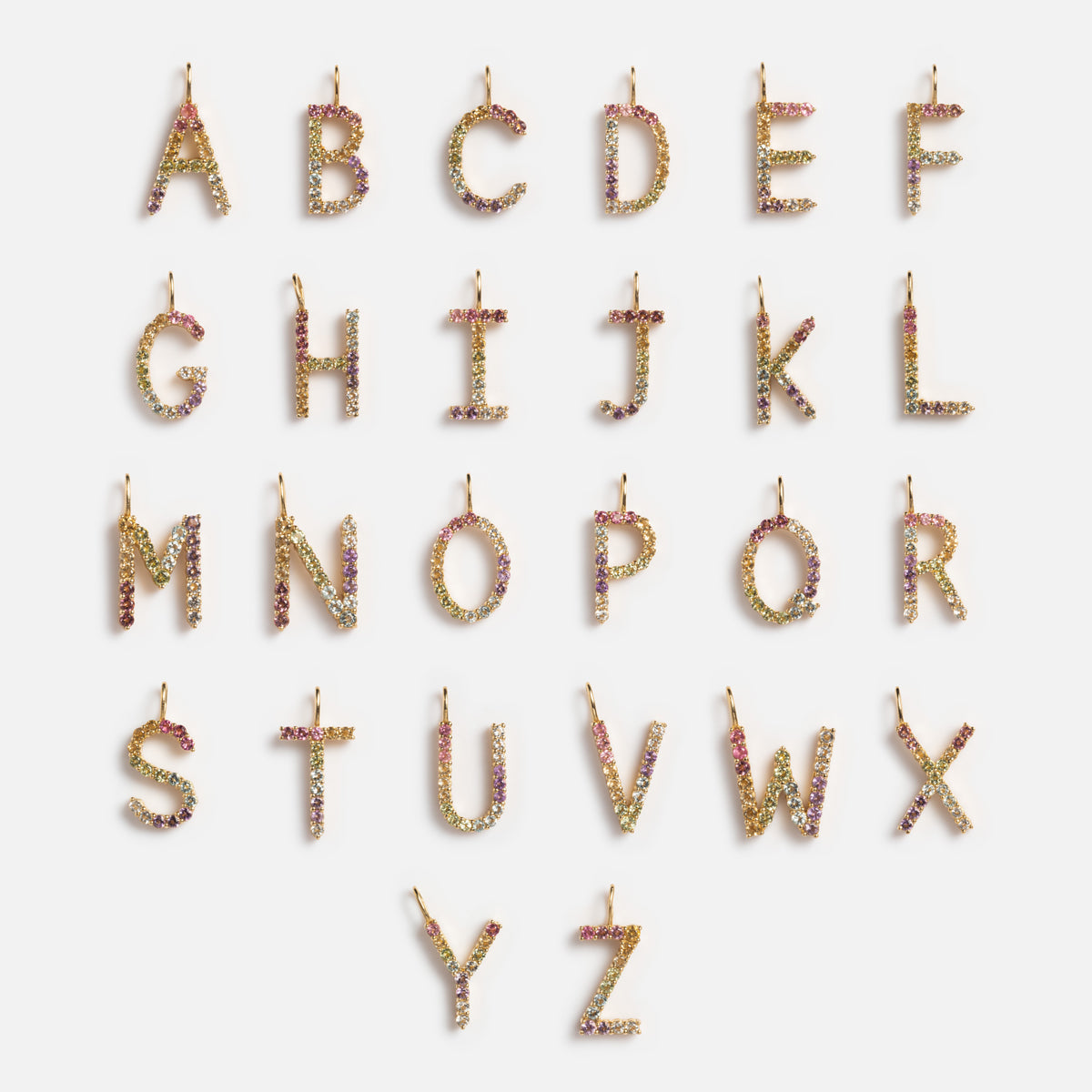 Solid Gold Pastel Gemstone Letter Charms arranged in four rows on a white background. Each charm sparkles with colorful stones and features a small loop at the top for attaching to a necklace or bracelet.