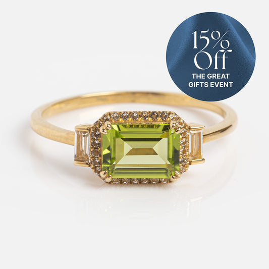 The Solid Gold Vintage Inspired East West Peridot Ring features a rectangular green gemstone and small diamonds on a white background. A blue tag says “15% Off THE GREAT GIFTS EVENT.” Ideal for vintage ring fans and Family Gold enthusiasts.