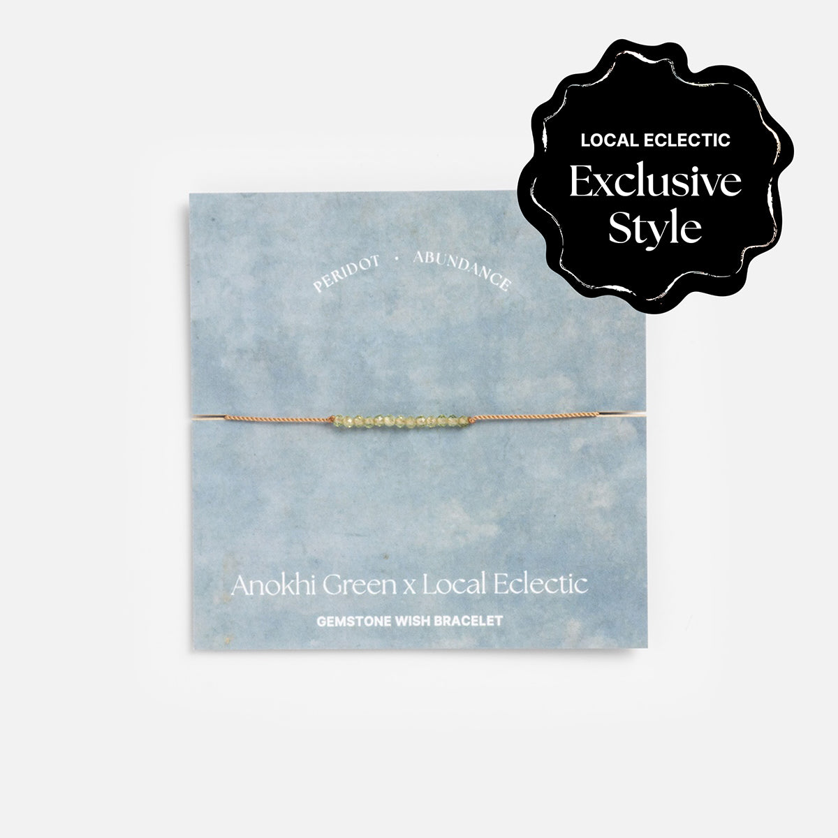 The Anokhi Green x Local Eclectic Gemstone Wish Bracelet with small green peridot gemstones rests on a pale blue background and exclusive card, featuring “Exclusive Style” and “PERIDOT - ABUNDANCE” in sparkling text.