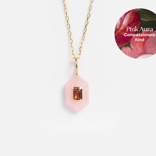 The Solid Gold Aura Necklace features a hexagonal pink pendant with a rectangular center gemstone. The inset reads: Pink Aura, Compassionate, Kind on swirling pink and green art.