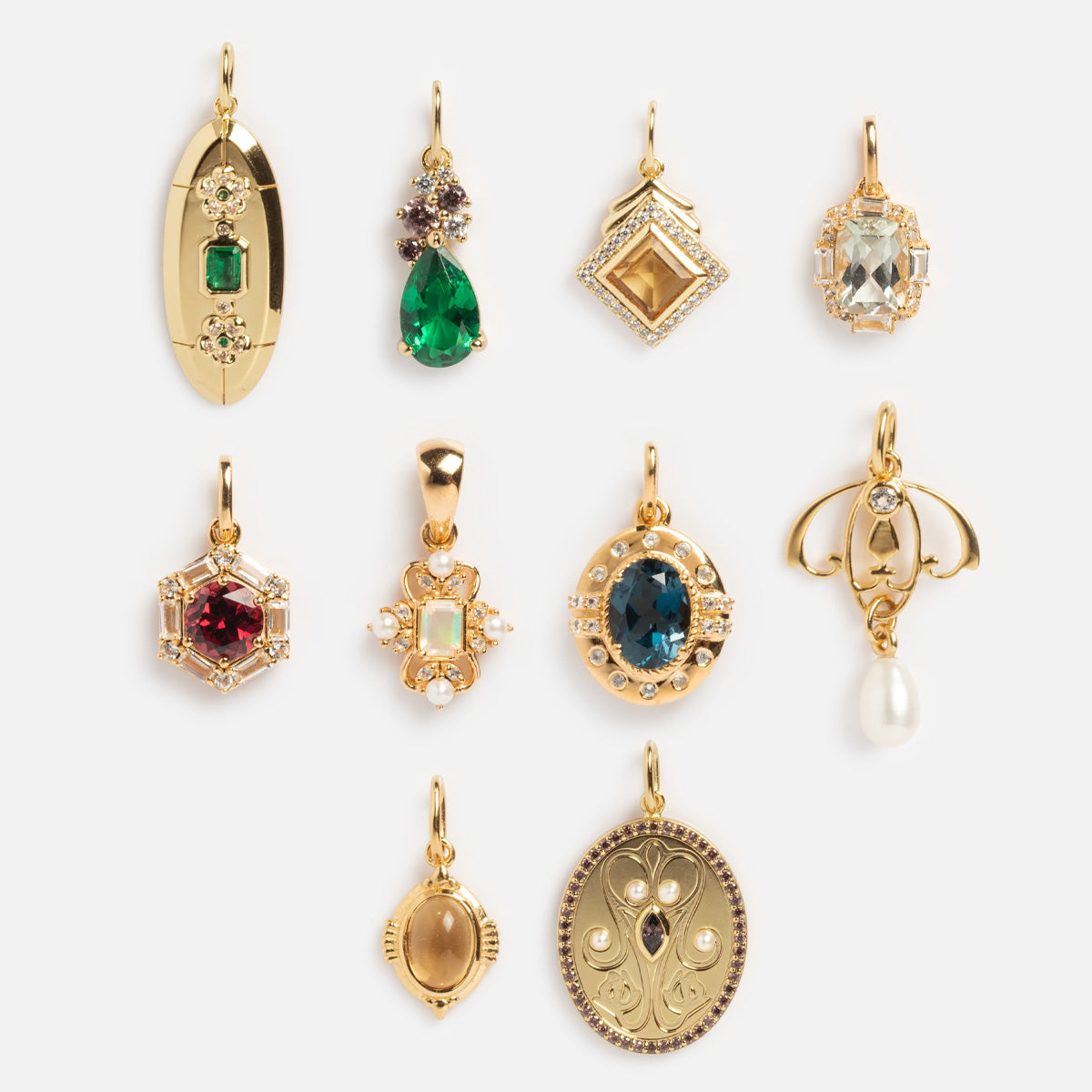 Nine Vintage Inspired Pendant Charms in gold vermeil with unique shapes and colored gemstones—emerald, ruby, blue—plus one with a dangling pearl. Each ornate pendant features distinct gemstone charm details, shown on a white background.