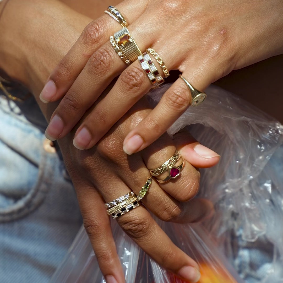 A close up of a woman's hands wearing several solid gold gemstone rings stacked